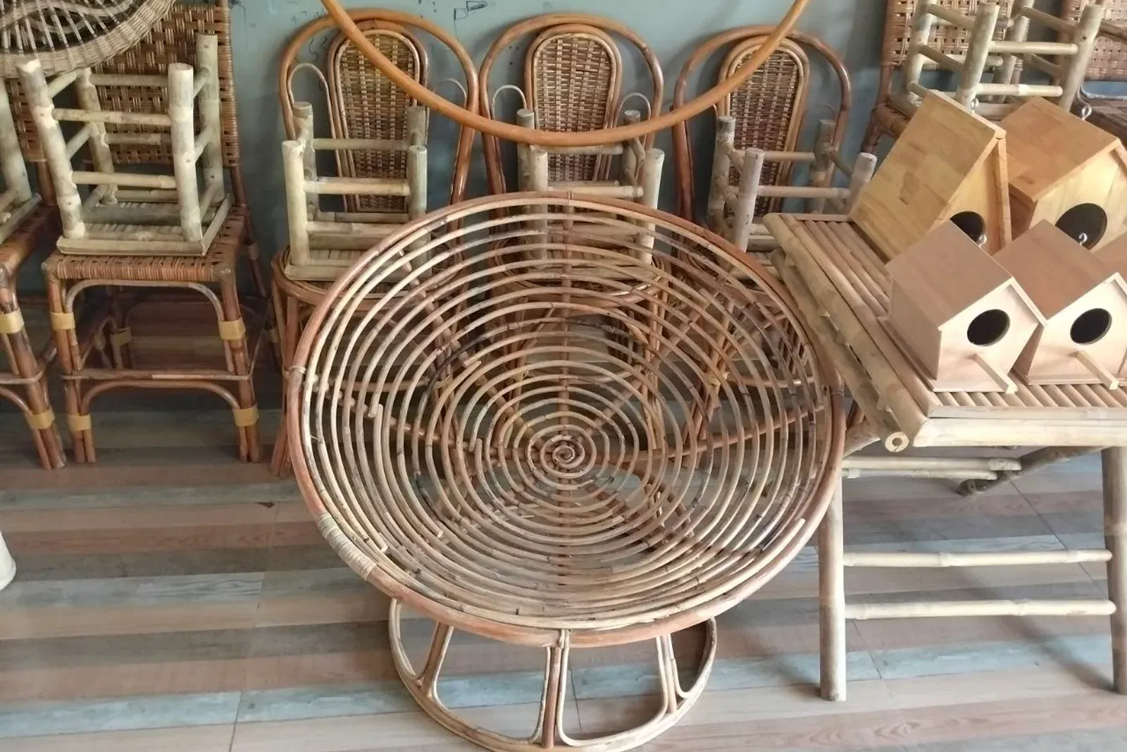 Rattan chairs against a wall next to a round papasan chair frame and wooden birdhouses